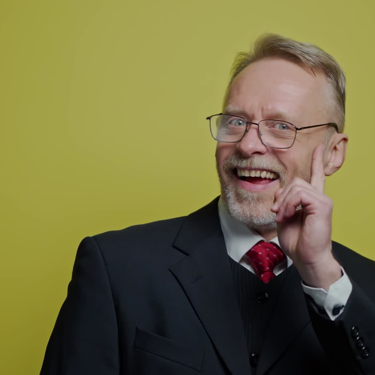 Positive businessman showing different emotions. Mature man in glasses and elegant costume shows funny face on the camera on yellow studio background.