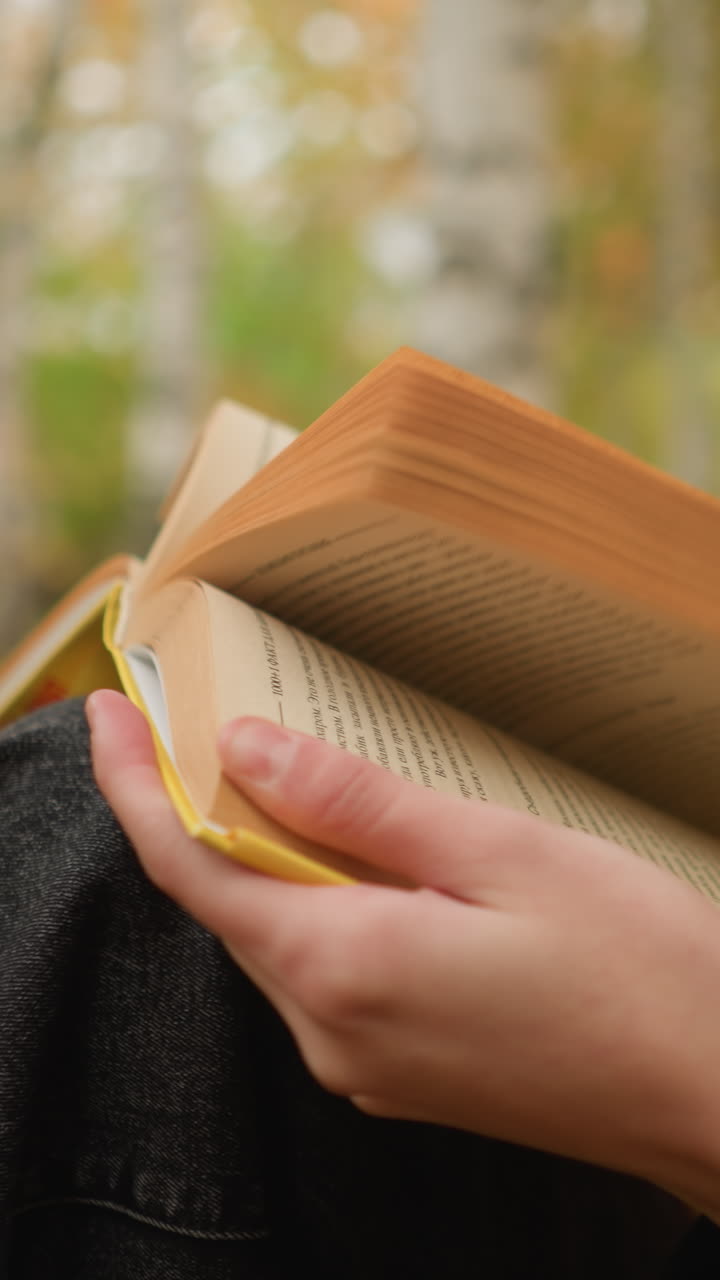 primer plano de una mujer con una bufanda amarilla volviendo las páginas del libro pensativamente, las hojas de otoño cubren el suelo mientras lee en un entorno al aire libre tranquilo, inmersa en el momento con enfoque