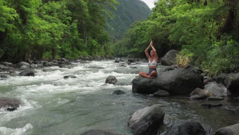 mujer haciendo meditación de yoga en roca al lado del río tropical en bali, sukhasana