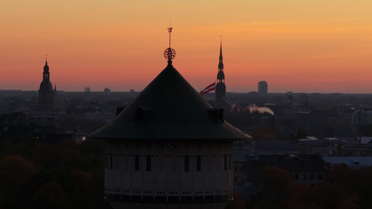 Złoty świt rysuje sylwetki Wieży Ciśnień Alises, podczas gdy w tle wznoszą się wieże Starego Miasta Rygi