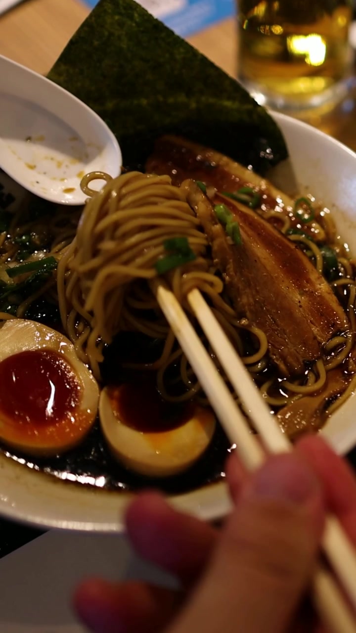 Seseorang makan ramen dengan sumpit di meja