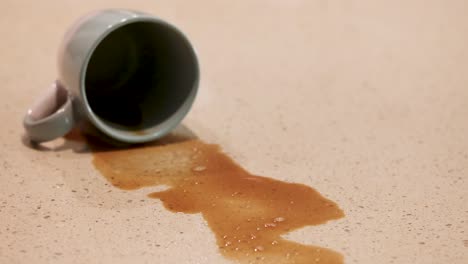 a hand uses a spray bottle to clean a coffee spill from a tipped mug on a table