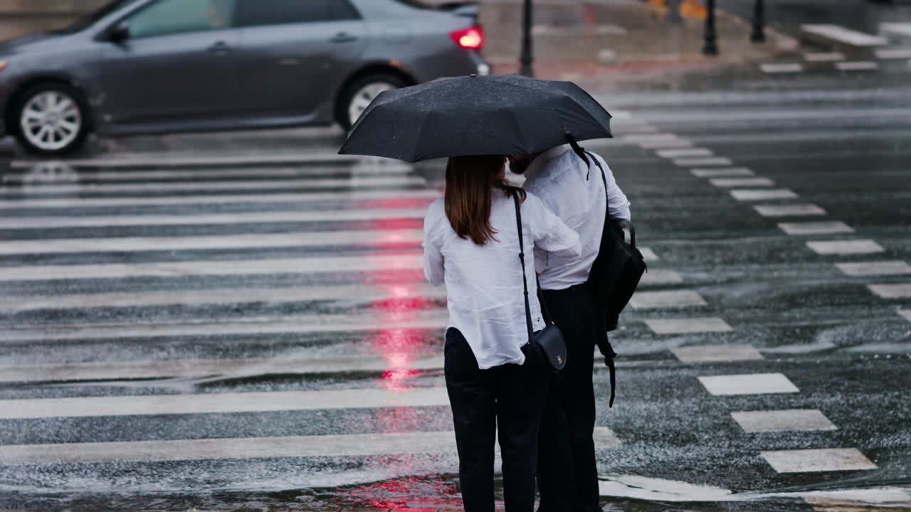Two girls holding an umbrella waiting at a pedestrian crossing on a rainy day in Chisinau, Moldova