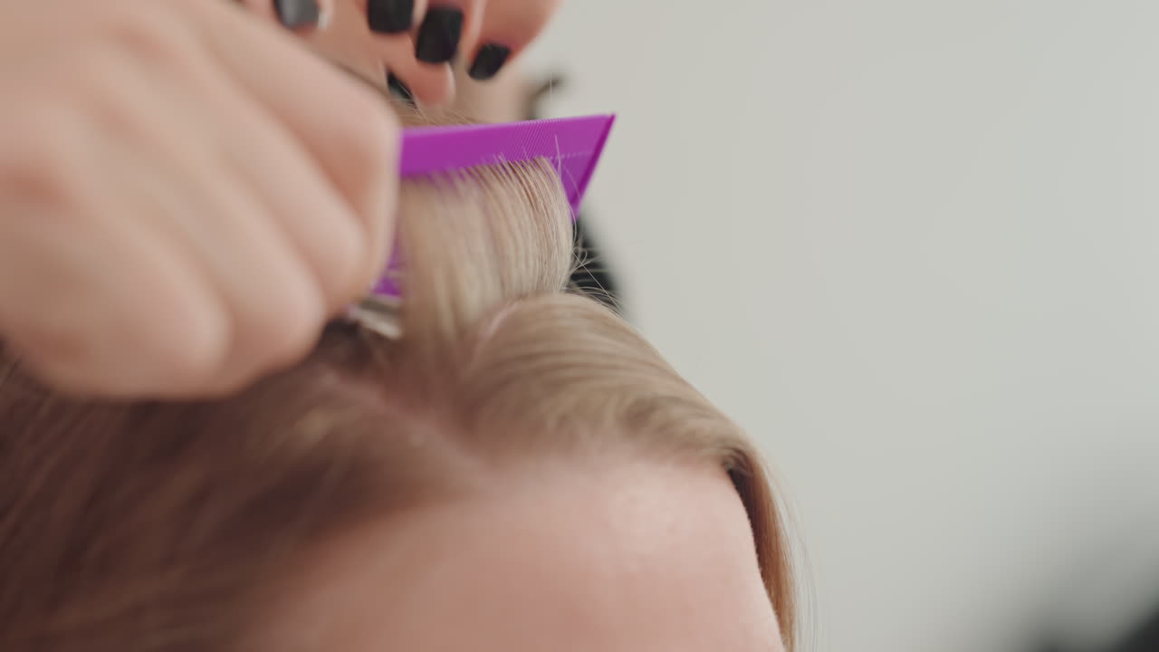 Nahaufnahme einer kaukasischen Frau, bei der ein professioneller Colorist beim Abteilen der Haare mit Folie Bleichmittel und Toner mit Folie aufträgt, der Stylist kämmt die Wurzeln, präziser Scheitel, Glättung, neutraler Studiohintergrund, ruhige, konzentrierte Atmosphäre