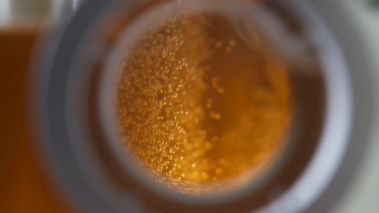 Primo piano di liquido ambrato che si muove all'interno di una bottiglia di vetro trasparente, con riflessi scintillanti, riflessi morbidi e uno sfondo sfocato che crea un aspetto astratto e caldo