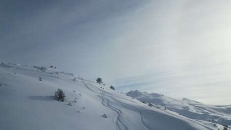 Aerial-epic-snow-covered-glacier-mountain-range-scenery,-fllying-over-alpine-summits-with-ski-tracks-on-sunny-day-winter