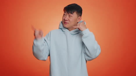 Handsome-asian-man-looking-at-camera-doing-phone-gesture-like-says-hey-you-call-me-back-conversation