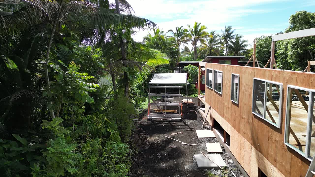 Drone flies alongside wooden house under construction, framed walls and jungle in Big Island, Hawaii.