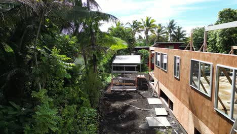 drone flies alongside wooden house under construction, framed walls and jungle in big island, hawaii.