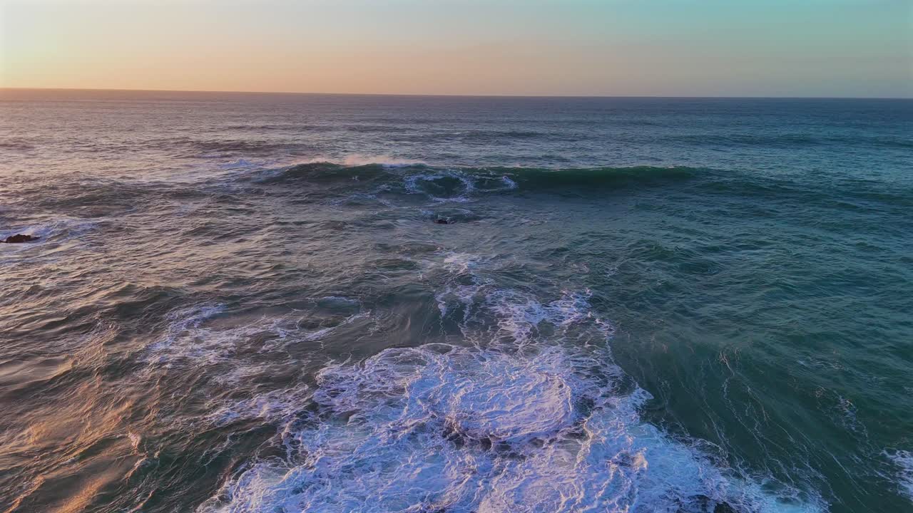 Onda oceanica pulita che si infrange in mare aperto con tenui tonalità del tramonto.
