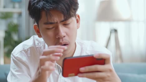 Close Up Of Asian Man Being Upset Losing Game On Smartphone While Sitting On Sofa In The Living Room