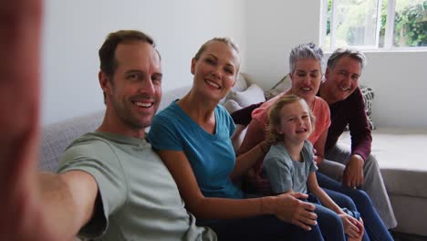 caucasian parents, grandparents and grandchildren taking selfie sitting on couch smiling