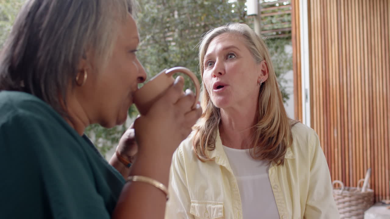 Enjoying coffee, multiracial senior female friends having friendly conversation outside, at home