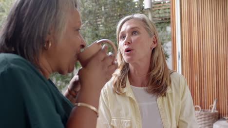 enjoying coffee, multiracial senior female friends having friendly conversation outside, at home