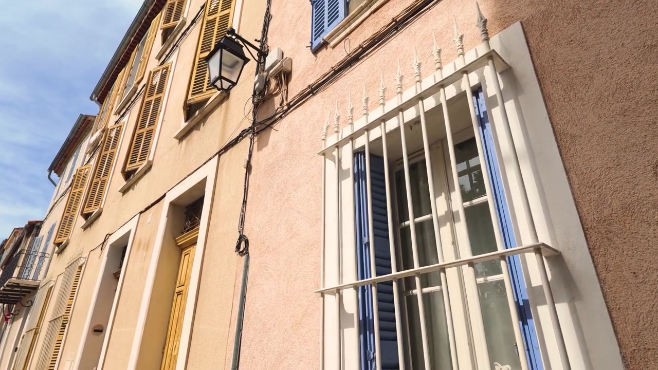 木製のシャッターとドアを備えた伝統的なパステルカラーの建物を、ローアングルカメラがパンして捉える。