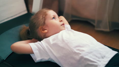 tired toddler in sportswear lies on treadmill in light room