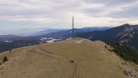 Drone-pullback-as-SUV-car-drives-up-along-winding-dirt-road-to-electrical-tower