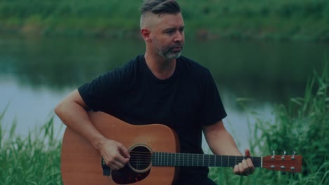 man playing acoustic guitar by a river
