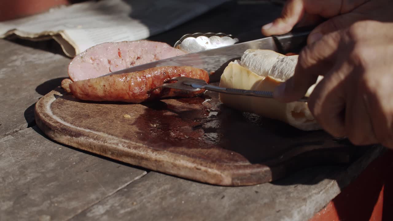 4K at 60fps (slow motion) - Man cutting a roasted sausage on a sunny day - BBQ (asado) - Relax and warm mood