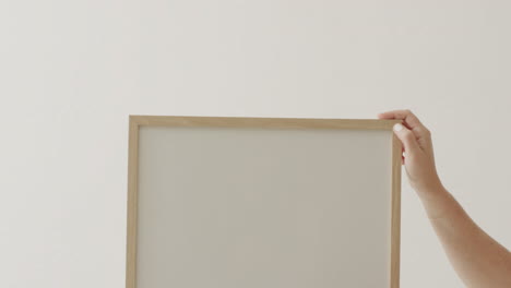 manos de una mujer caucásica sosteniendo un marco con espacio de copia en fondo blanco contra una pared blanca