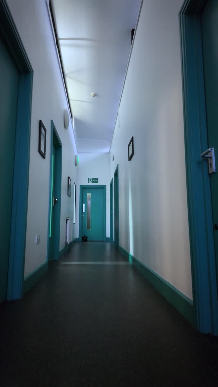 POV da angolazione bassa di un corridoio d'ospedale vuoto con porte color verde acqua e pavimento scuro, caratterizzato da una prospettiva centrale e un'architettura pulita per concetti medici