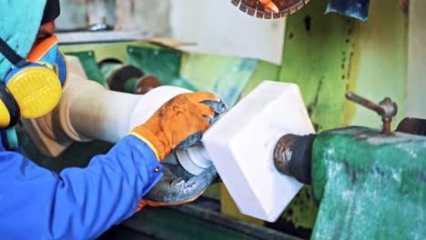 Worker man in special uniform with mask polishing stone in workshop. Man is standing at the grinder machine and polishing stone. Camera moves forward.