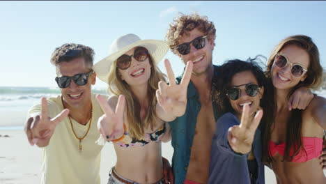 grupo de amigos sonriendo y haciendo una señal de paz en la cámara para un retrato en la playa