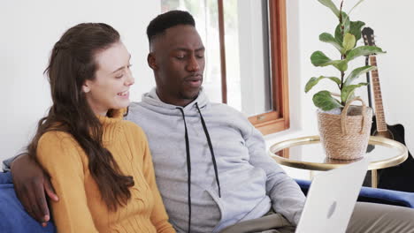 Happy diverse couple sitting on sofa and using tablet in home,copy space