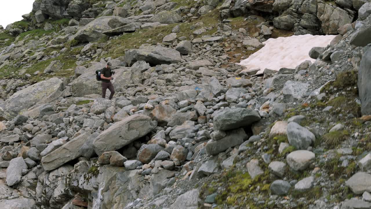 A hiker ascends through rocky terrain near the Fellaria Glacier in Valmalenco, Alps. Drone video captures the rugged landscape and the pedestal up movement highlights the challenging environment