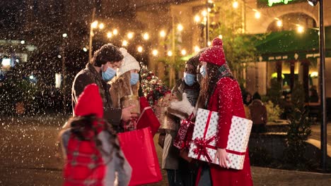 Felices-Amigos-Multiétnicos-Hablando-Y-Sosteniendo-Regalos-En-La-Calle-Mientras-Nieva-En-Navidad