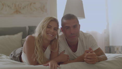 happy man and woman lying on bed at home and looking at camera