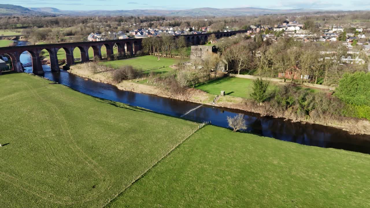 Il filmato del drone cattura Bolton Abbey con prati vivaci, un fiume sereno e un villaggio distante. La vegetazione lussureggiante e i cieli sereni creano un'atmosfera tranquilla dall'alto nel North Yorkshire.