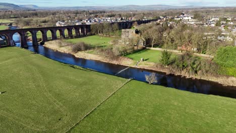 drone footage captures bolton abbey with vibrant meadows, serene river, and distant village. lush greenery and clear skies create a tranquil atmosphere from above in north yorkshire