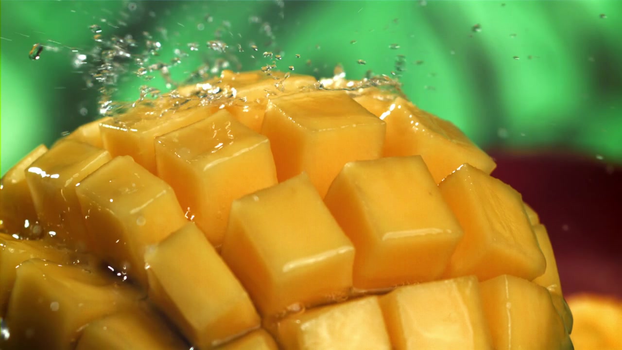 Zbliżenie na wodę rozpryskującą się na świeżych kostkach mango.