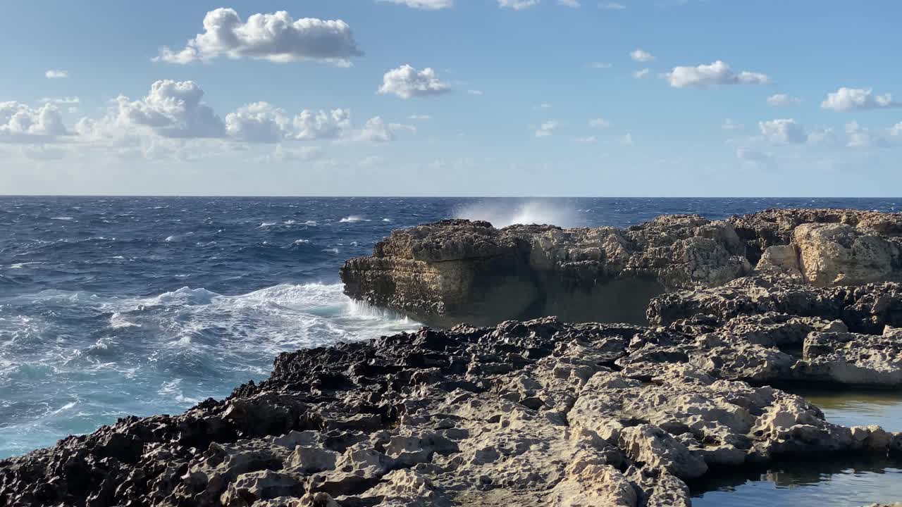 el cielo azul con cúmulos dispersos se encuentra con el océano inquieto salpicando la costa rocosa