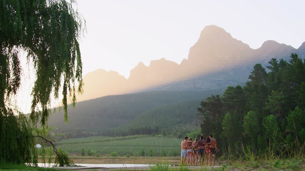 Adult friends standing on a distant jetty in lake, back view