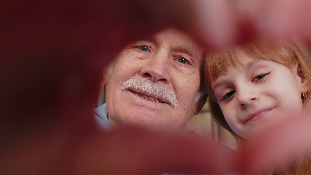Grandfather granddaughter making symbol of love showing heart sign to camera happy smiling family