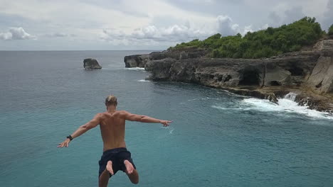 following aerial as young man leaps off cliff into bali sea far below