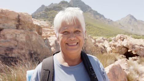 Portrait-of-happy-senior-biracial-woman-in-mountains-with-backpack,-in-slow-motion