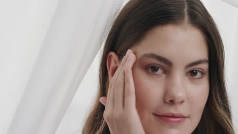 retrato de una hermosa mujer joven masajeando las sienes acariciando una piel suave y saludable tocando la cara con las manos disfrutando de una tez natural suave belleza femenina en fondo blanco