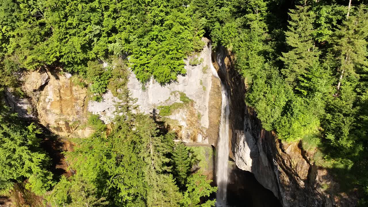 A powerful stream of water creates the Bergli Stüber Waterfall, plunging from a large grotto carved into the rocky cliffs of Fätschbach in Glarus Süd, Switzerland
