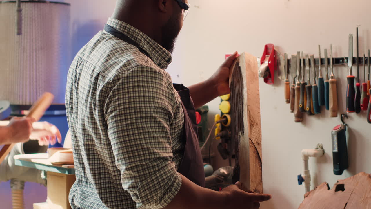 Cabinetmaker evaluates timber block, picking right tool from rack