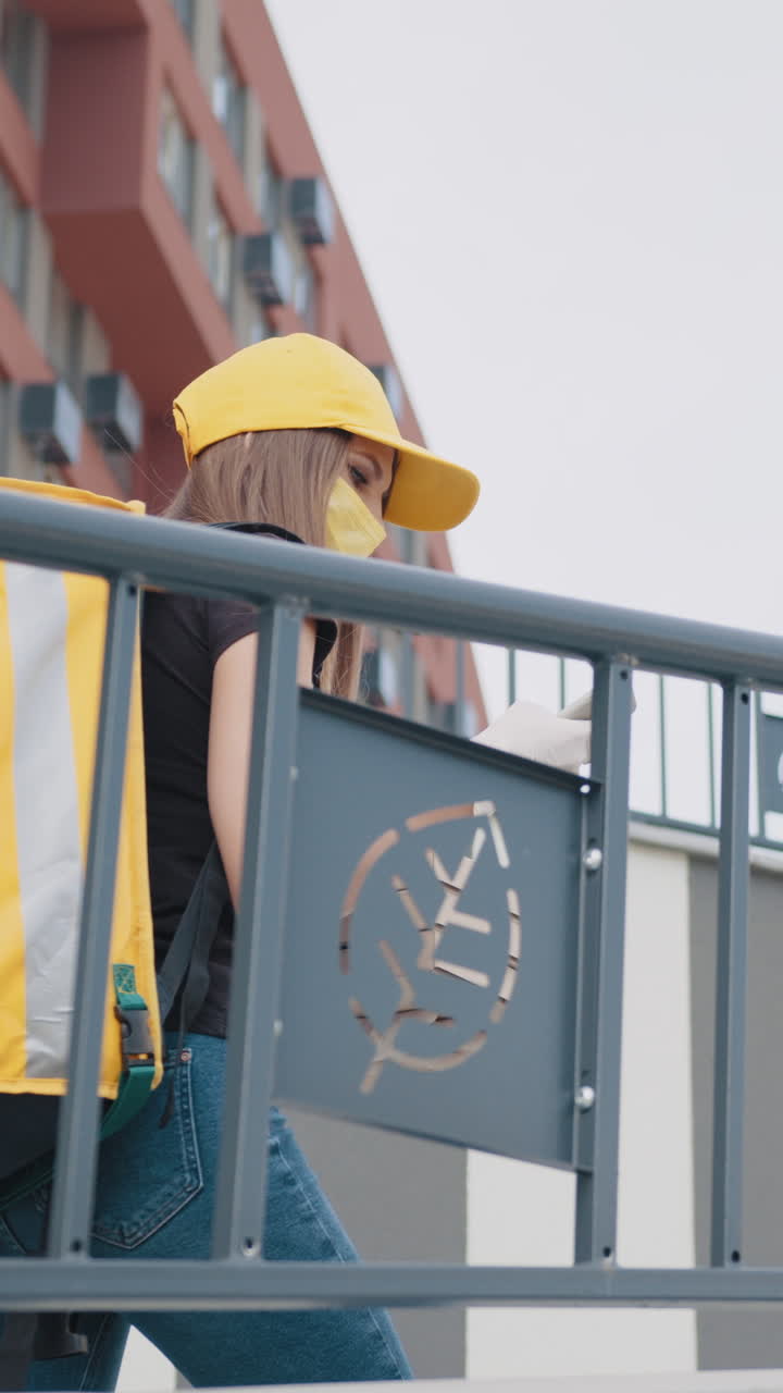 Delivery person with pizza boxes checking her phone outside a building