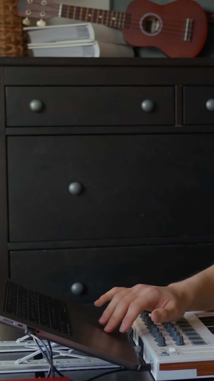 Person creating music on a keyboard in a cozy room with a ukulele