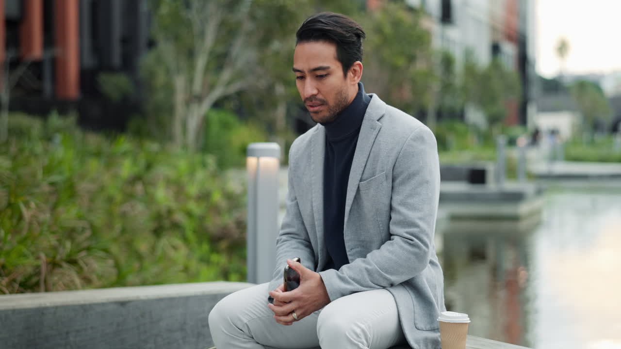 A man in a suit is sitting on a bench looking at his phone.