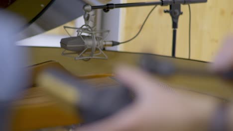 micrófono de condensador colocado sobre las cuerdas de un piano de cola de concierto abierto mientras otro ya está colocado