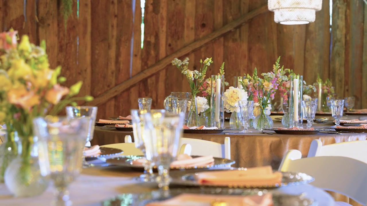 Charming rustic barn wedding reception setup featuring tables with elegant glassware, fresh floral centerpieces, soft golden lighting, and wooden walls for a cozy, romantic atmosphere.