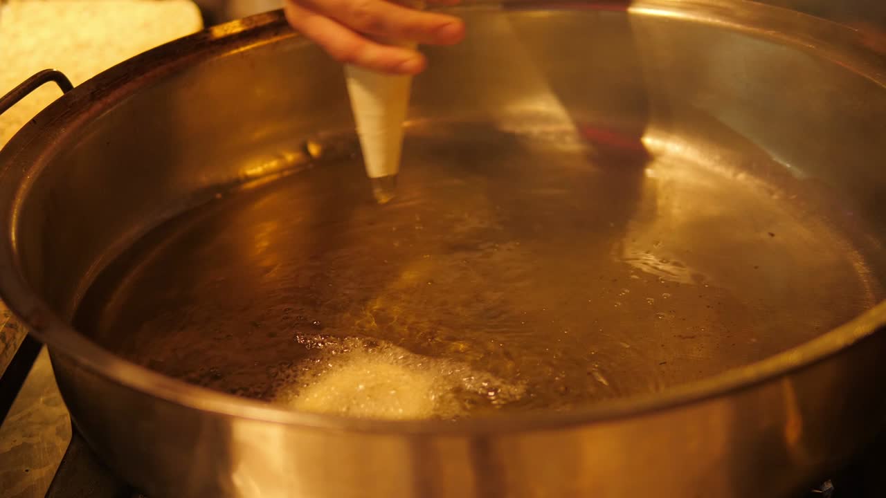 Close-up of the chef squeezing the dough out of the pastry bag into the oil.