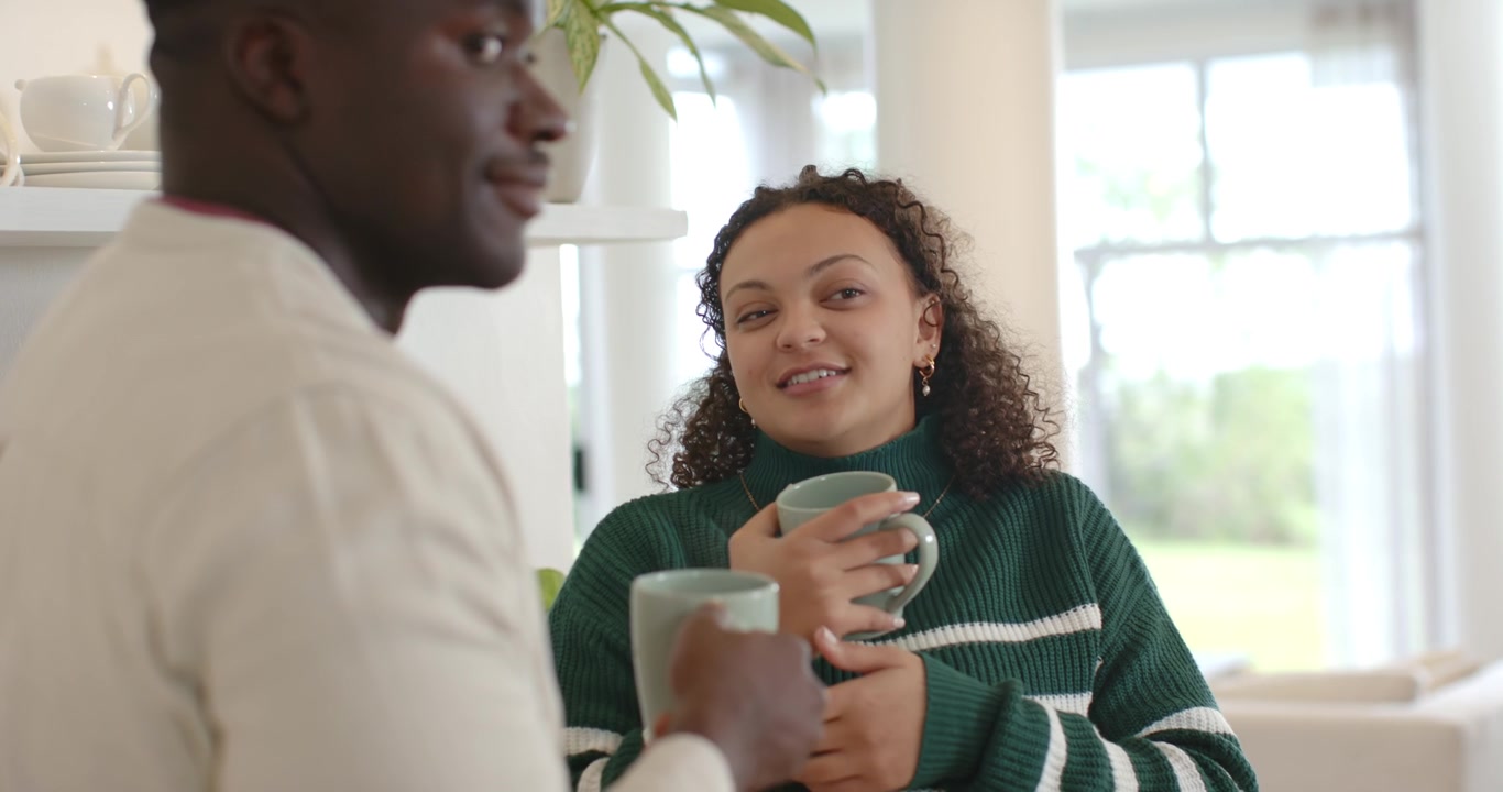 Couple standing in bright kitchen living area, woman starting conversation while cradling mint mugs
