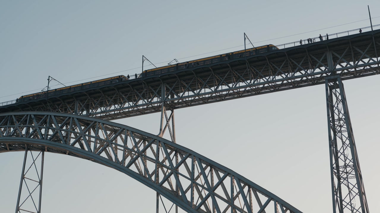 Yellow metro train moving across the iconic iron bridge with pedestrians in Porto, Portugal.